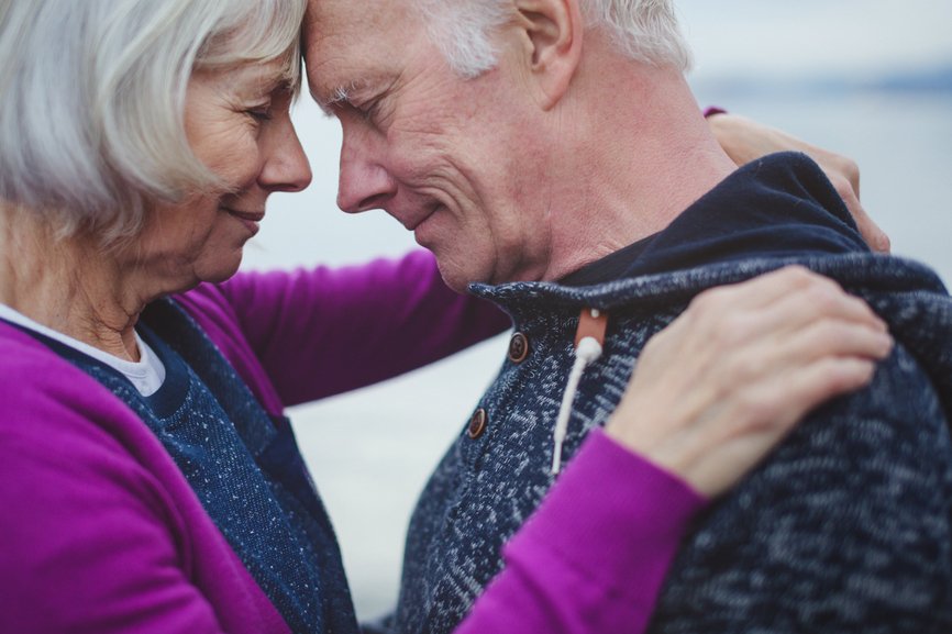 Sincere senior couple leaning foreheads together outside near wa