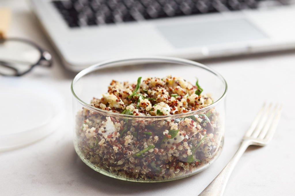 Close-up of healthy quinoa salad with goat cheese, olives, goat cheese dressed with olive oil on desk in office.